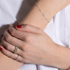 Close-up of a person's wrist with a white gold diamond station bracelet, ring, and nail polish on a white background