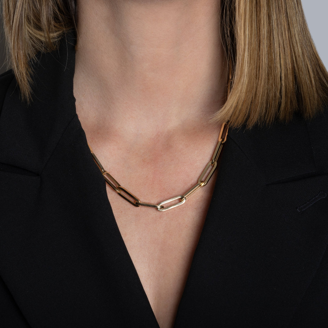 A person wearing a 14k gold chunky paperclip chain and a black blazer. 