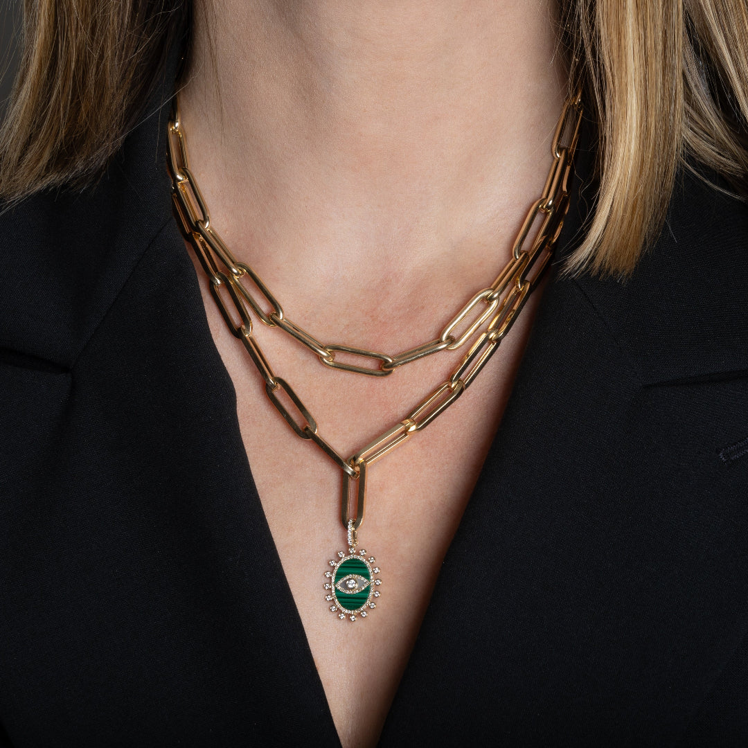 A person wearing two 14k gold chunky paperclip chains that are layered, one features a malachite and diamond pendant.