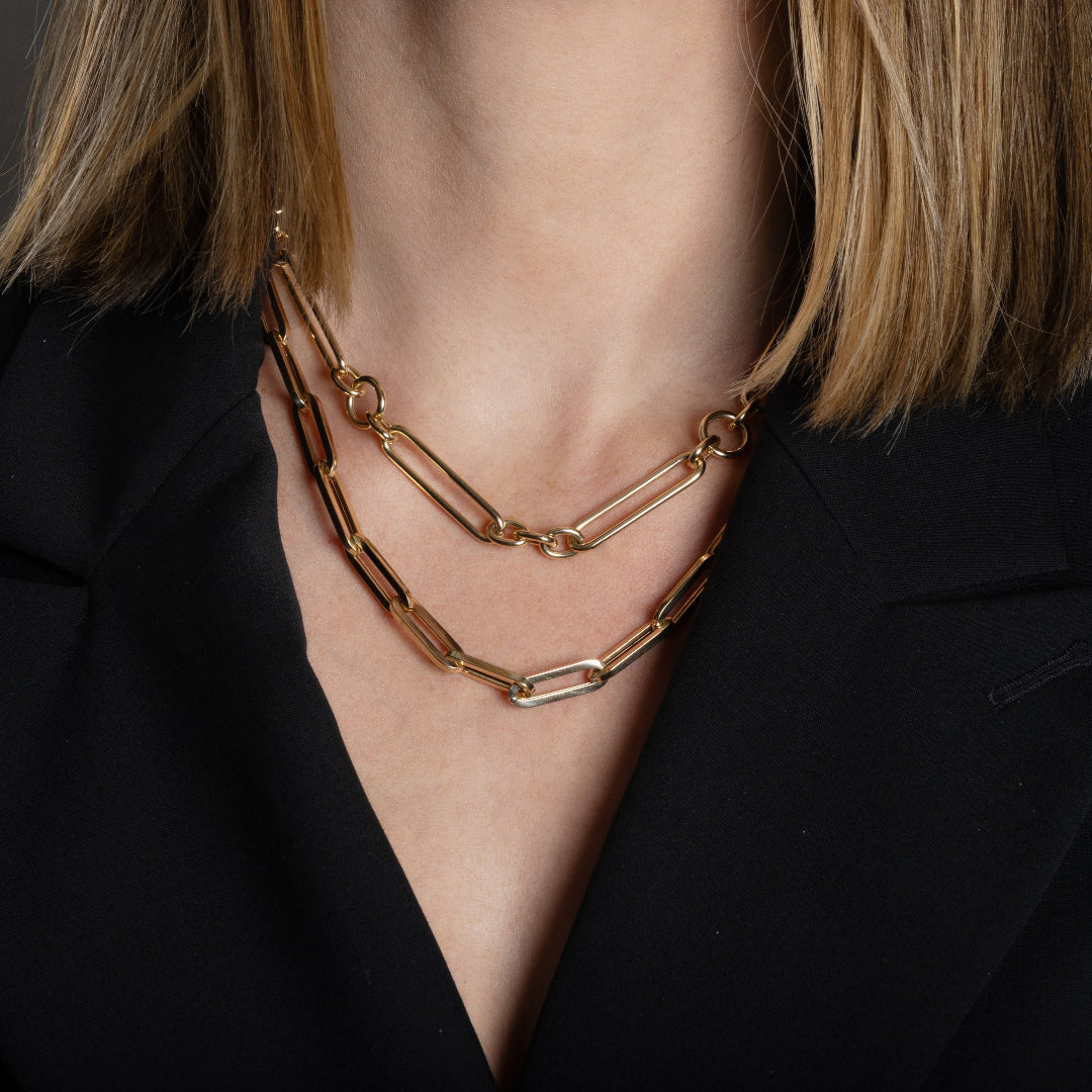 A person wearing two chunky 14k gold necklaces and a black blazer. 