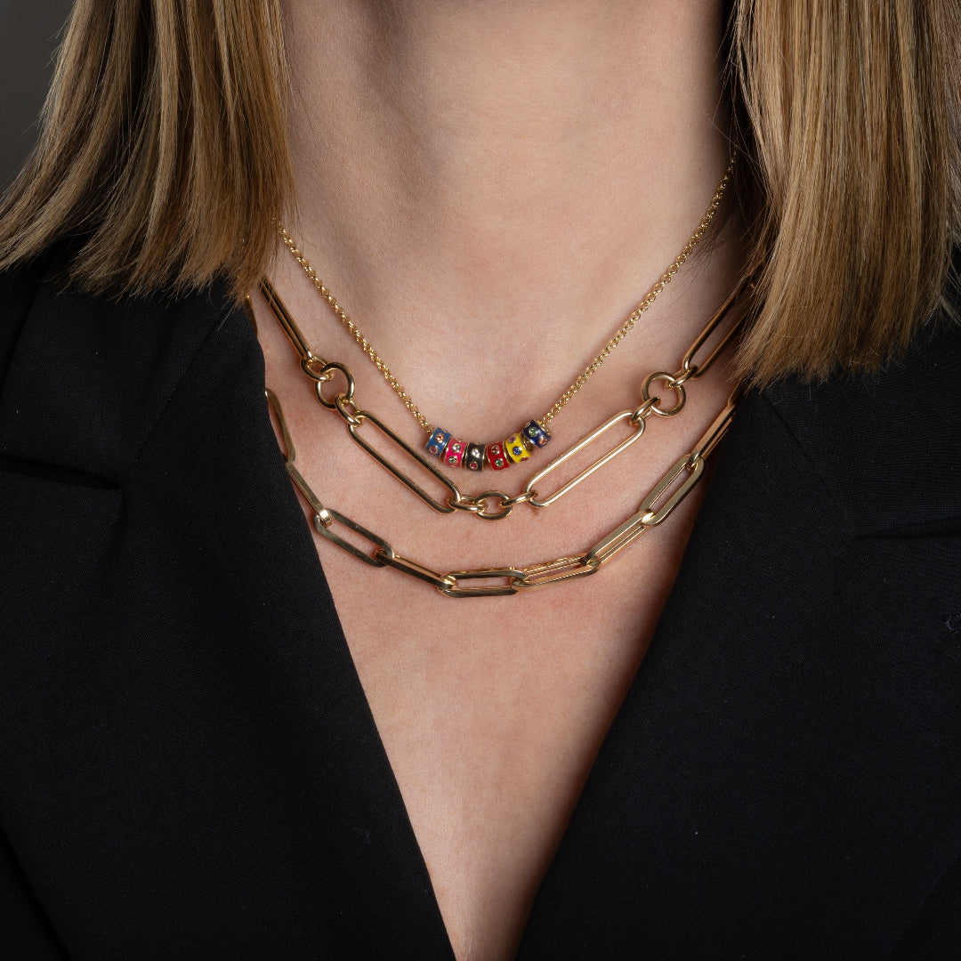 A person wearing two chunky 14k gold necklaces and one mini rolo chain with colored enamel beads. 