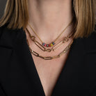 A person wearing two chunky 14k gold necklaces and one mini rolo chain with colored enamel beads. 