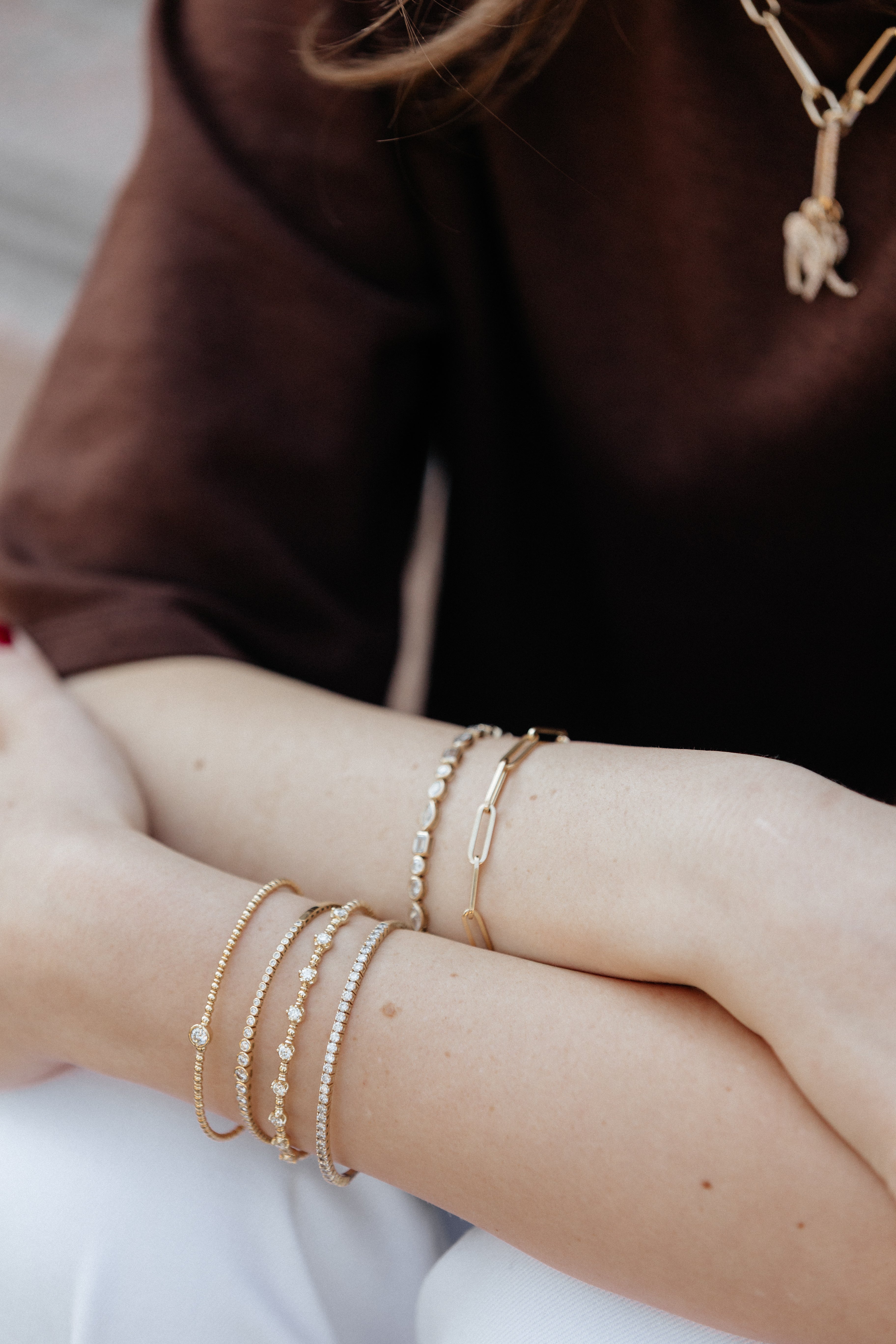 Close-up of a person's arms with gold bracelets and a necklace on a neutral background