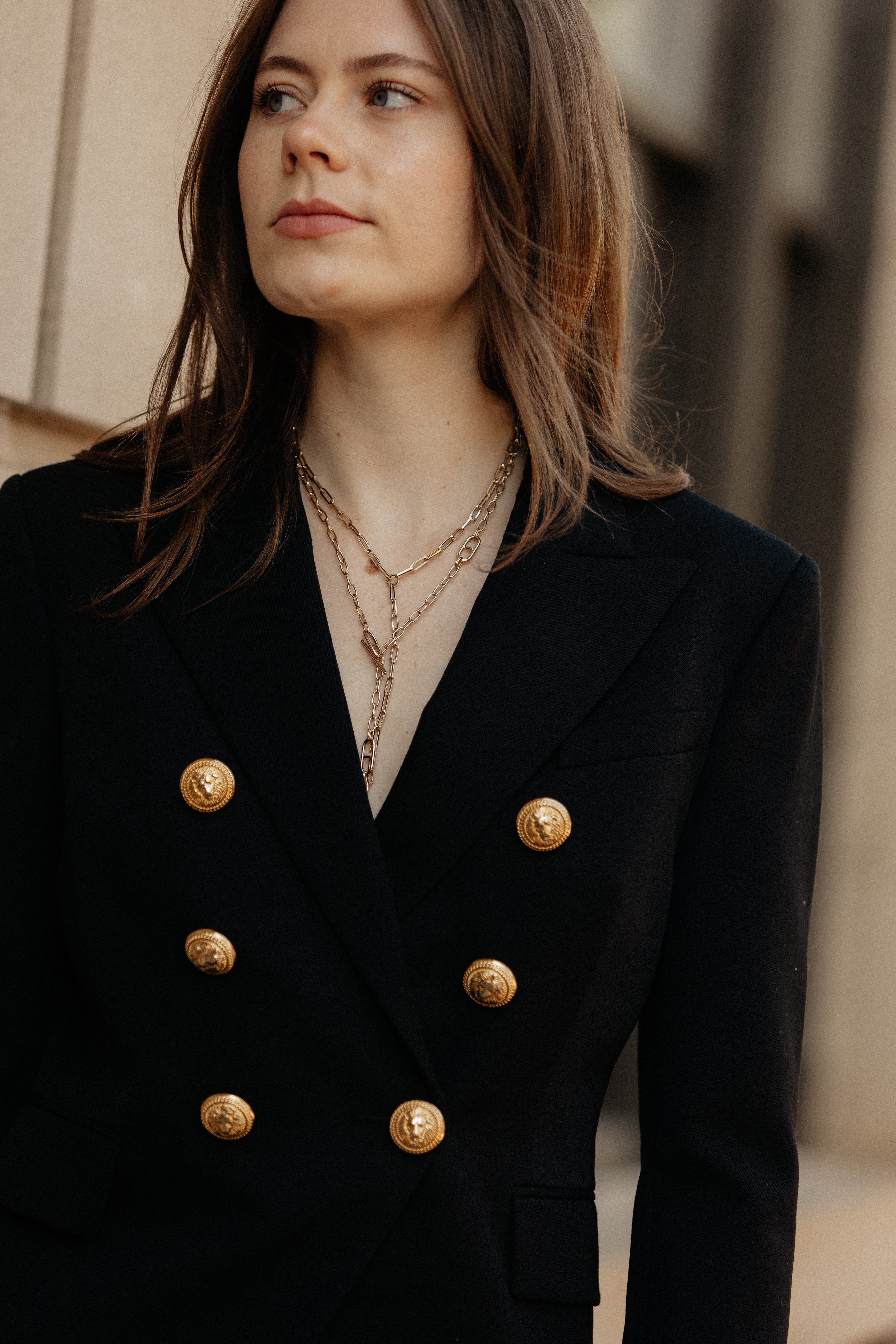 Woman wearing a black double-breasted jacket with gold buttons against a blurred background.