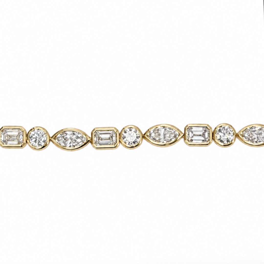 A close-up of a yellow gold tennis bracelet featuring a continuous row of round, emerald-cut, and marquise-cut diamonds on a plain white background.