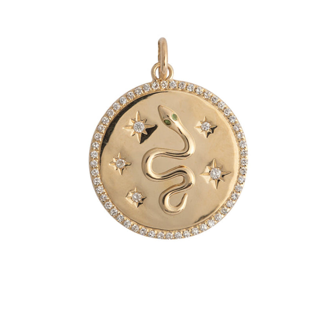A 14k gold diamond pendant with a serpentine design, featuring emerald eyes and star details, surrounded by a circular band with diamond embellishments.