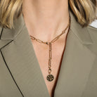 A 14k gold chain necklace with pendant worn by a person in a beige blazer.